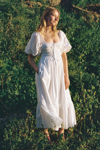Woman in a white dress standing in a natural setting with greenery.