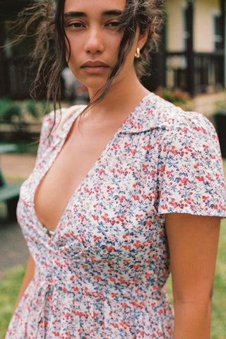 Woman standing outside looking at the camera, with a V-neck dress featuring a small blue and red floral pattern dress