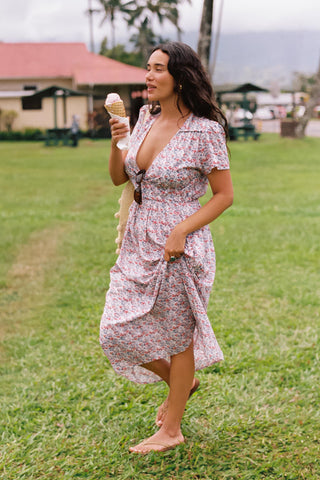 Woman eating ice cream, with a V-neck dress featuring a small blue and red floral pattern dress. The dress is just above ankle length. 