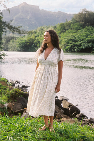Woman in a cream patterned dress standing by a lake with mountains in the background