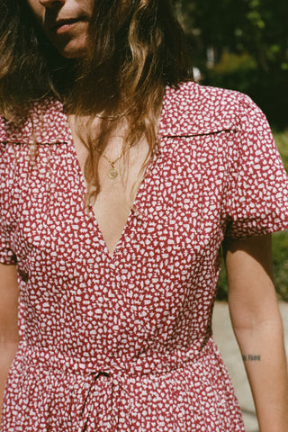 A close-up of a woman wearing a short-sleeve wrap-style dress with a red and white floral pattern, featuring a deep V-neckline and a drawstring waist.