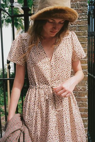 Women wearing a beige patterned
 dress with a cozy hat holding a plaid item